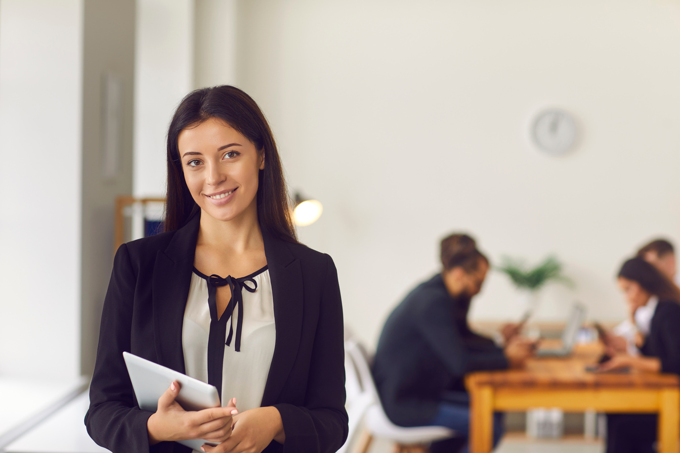 Happy Young Female Company President with Tablet in Hands Standing in Office Looking at Camera